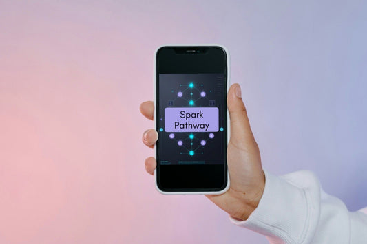 A hand holding a smartphone that displays the 'Spark Pathway' app against a soft pink and purple gradient background.