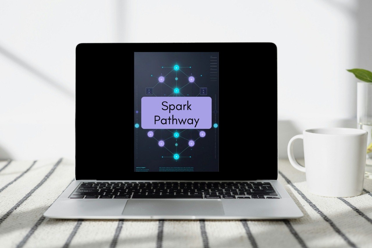 A silver laptop sits open on a striped fabric surface, displaying a dark screen with a purple card labeled 'Spark Pathway.' A white mug is to the right, and the scene is softly lit with natural shadows.